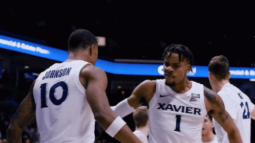 a basketball player wearing a xavier jersey shakes another player 's hand