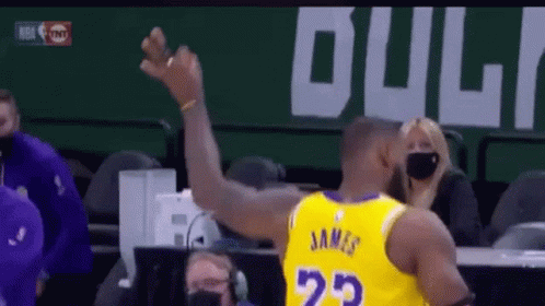 A Basketball Player Wearing A Yellow Jersey With The Number 23 On The Back Is Raising His Arm In The Air . GIF