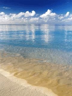 A Beach With A Blue Sky And Clouds Reflected In The Ocean GIF