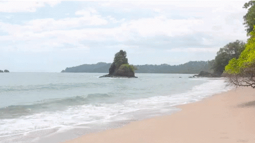 A Beach With A Large Rock In The Middle Of The Water GIF