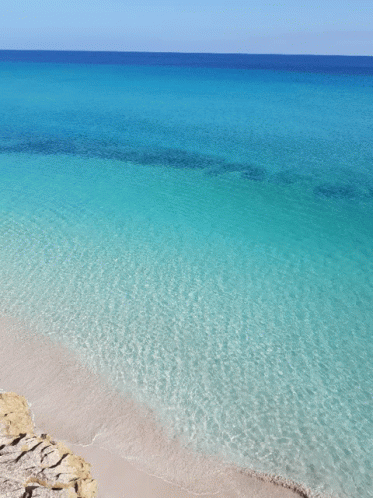 A Beach With Turquoise Water And A Blue Sky GIF