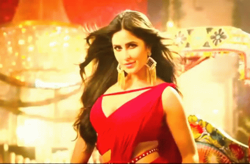 A Beautiful Woman In A Red Dress Is Standing In Front Of A Chandelier . GIF