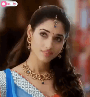 A Beautiful Woman Wearing A Necklace And Earrings Is Looking At The Camera . GIF