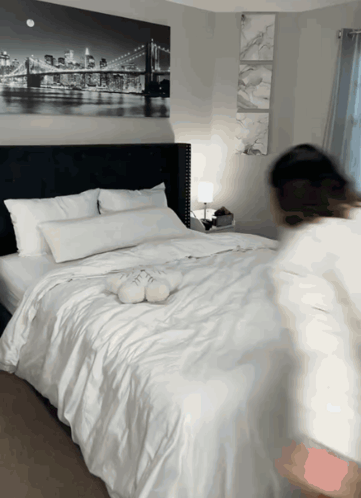 A Bed With White Sheets And Pillows In A Bedroom With A Painting Of A Bridge On The Wall GIF