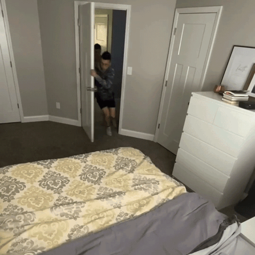 A Bedroom With A Bed And A Dresser And A Door GIF