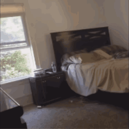 A Bedroom With A Bed And A Nightstand GIF