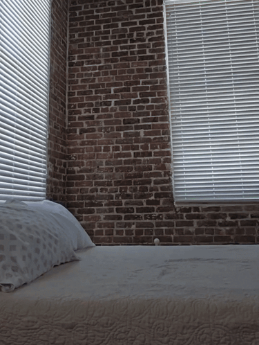 A Bedroom With A Brick Wall And Blinds GIF