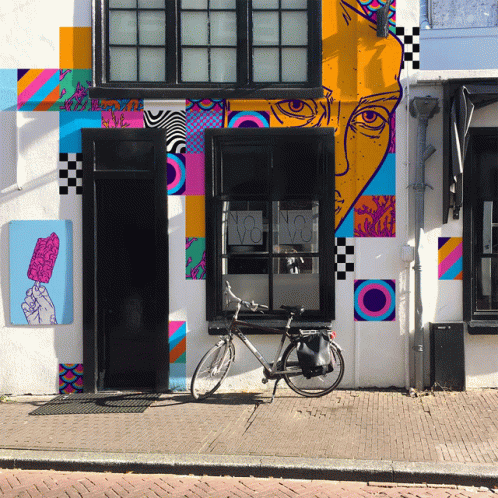 A Bicycle Is Parked In Front Of A Building With A Colorful Mural GIF