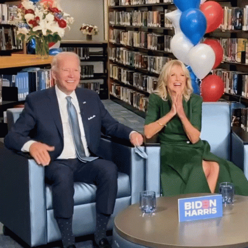 A Biden Harris Sign Sits On A Table Next To A Man In A Suit GIF