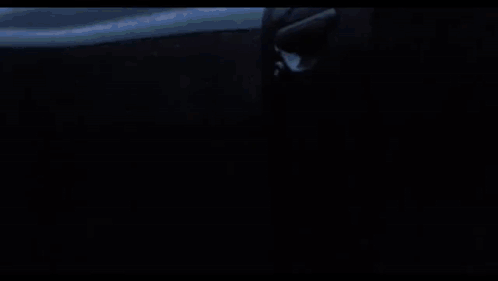 A Black Airplane Is Flying Through A Cloudy Sky . GIF