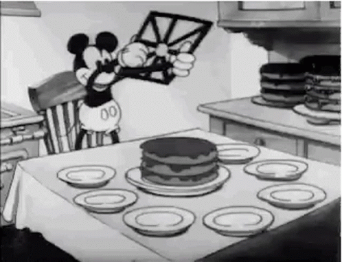 A Black And White Cartoon Of Mickey Mouse Sitting At A Table With A Cake . GIF
