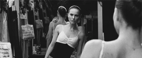 A Black And White Photo Of A Ballerina Looking At Herself In A Mirror . GIF
