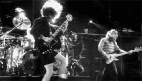 A Black And White Photo Of A Band Playing Guitars On Stage . GIF