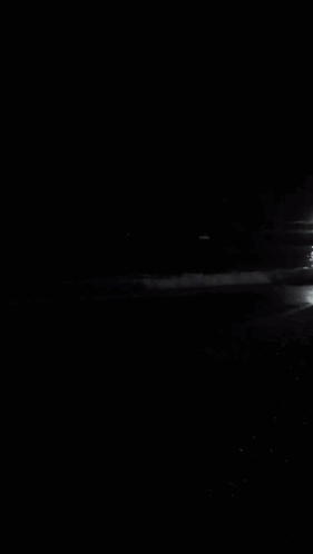 A Black And White Photo Of A Beach At Night With A Boat In The Distance GIF