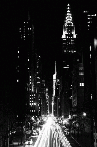 A Black And White Photo Of A City Street At Night With A Tall Building In The Background GIF
