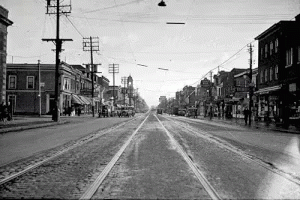 A Black And White Photo Of A City Street With A Train Going Down It GIF