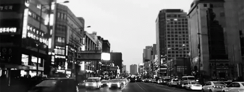 A Black And White Photo Of A City Street With Lots Of Cars And Buildings GIF