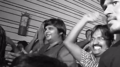 A Black And White Photo Of A Crowd With A Fire Extinguisher On The Wall Behind Them GIF