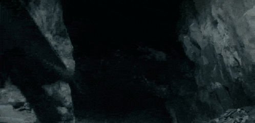 A Black And White Photo Of A Dragon Flying Over A Rocky Hillside . GIF