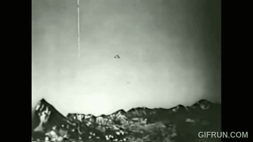 A Black And White Photo Of A Flying Object Over A Mountain Range . GIF