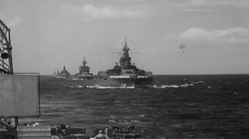 a black and white photo of a group of military ships in the ocean