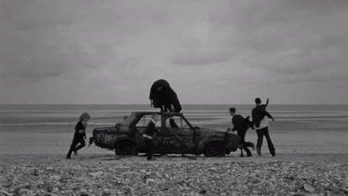 A Black And White Photo Of A Group Of People Standing Around A Car GIF