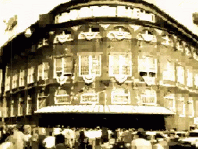 A Black And White Photo Of A Large Building With A Sign That Says ' Theatre ' On It GIF