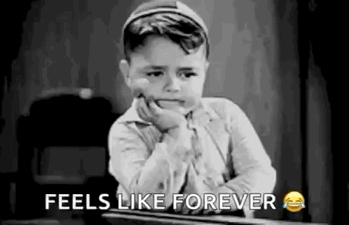 A Black And White Photo Of A Little Boy Sitting At A Desk With His Hand On His Face . GIF