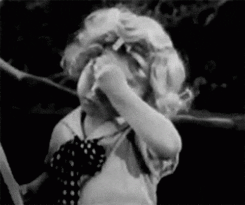A Black And White Photo Of A Little Girl Covering Her Face With Her Hands . GIF