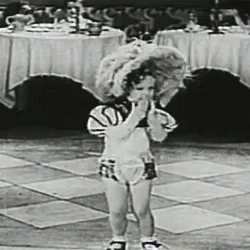 A Black And White Photo Of A Little Girl Standing On A Tiled Floor In Front Of A Table . GIF
