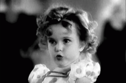 A Black And White Photo Of A Little Girl Wearing A Dress And A Headband . GIF