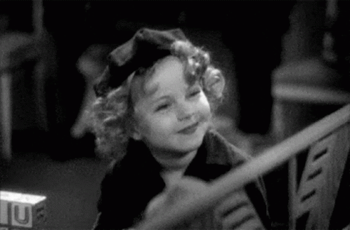A Black And White Photo Of A Little Girl Wearing A Hat . GIF