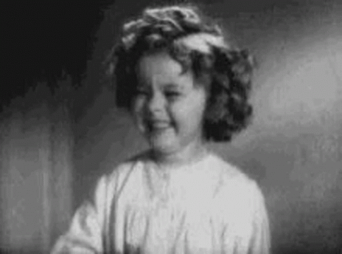 A Black And White Photo Of A Little Girl With Curly Hair Smiling . GIF