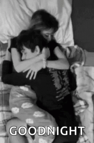 A Black And White Photo Of A Man And A Woman Hugging Each Other In Bed . GIF