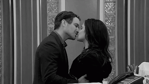 A Black And White Photo Of A Man And A Woman Kissing In An Office . GIF