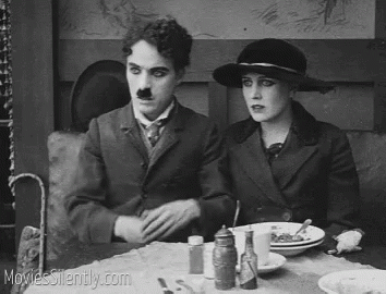 A Black And White Photo Of A Man And A Woman Sitting At A Table . GIF