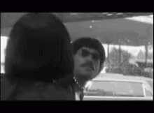 A Black And White Photo Of A Man And A Woman Standing Next To Each Other In A Car . GIF