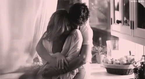 A Black And White Photo Of A Man And Woman Hugging In A Kitchen . GIF