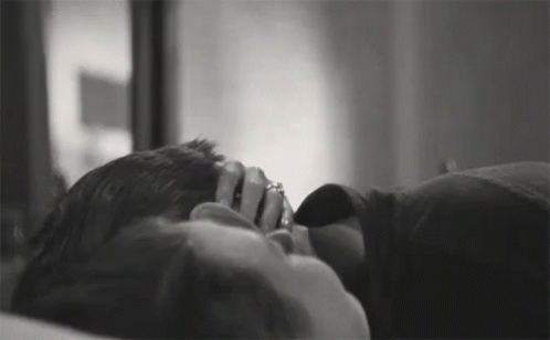 A Black And White Photo Of A Man And Woman Laying On A Bed . The Woman Is Wearing A Ring On Her Finger . GIF