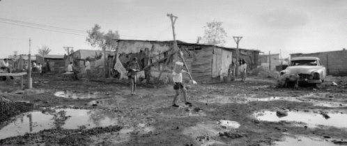 A Black And White Photo Of A Man Carrying A Bucket Of Water In A Muddy Area . GIF