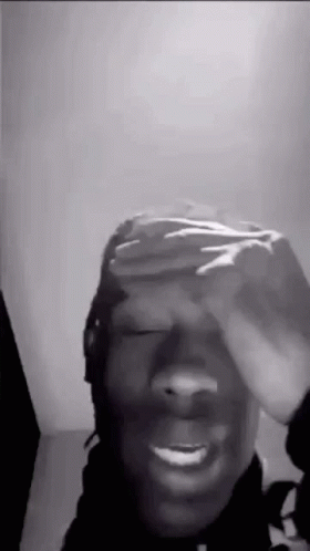 A Black And White Photo Of A Man Covering His Eyes With His Hand . GIF