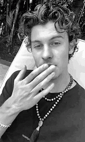 A Black And White Photo Of A Man Covering His Mouth With His Hands While Wearing A Necklace . GIF