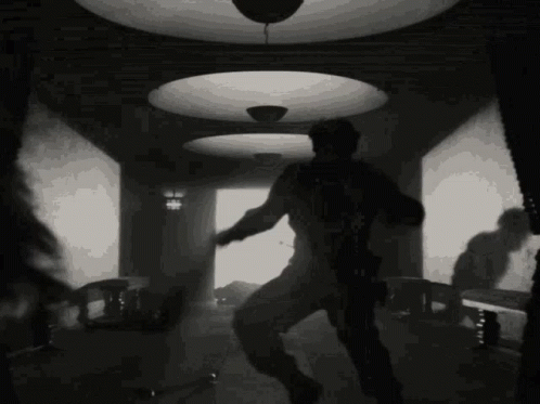 A Black And White Photo Of A Man Dancing In A Room With A Ceiling Light . GIF
