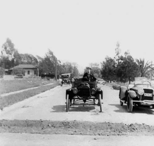 A Black And White Photo Of A Man Driving An Old Car GIF