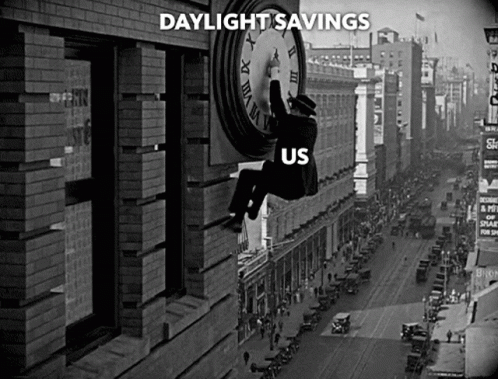 A Black And White Photo Of A Man Hanging From A Clock That Says Daylight Savings Us GIF