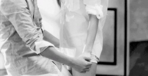 A Black And White Photo Of A Man Helping A Woman Tie Her Shirt . GIF
