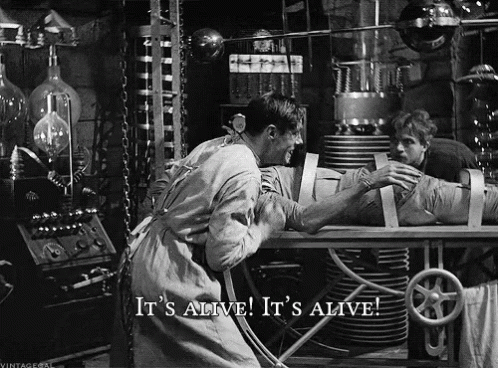 A Black And White Photo Of A Man Holding A Mummy With The Caption It 'S Alive It 'S Alive GIF