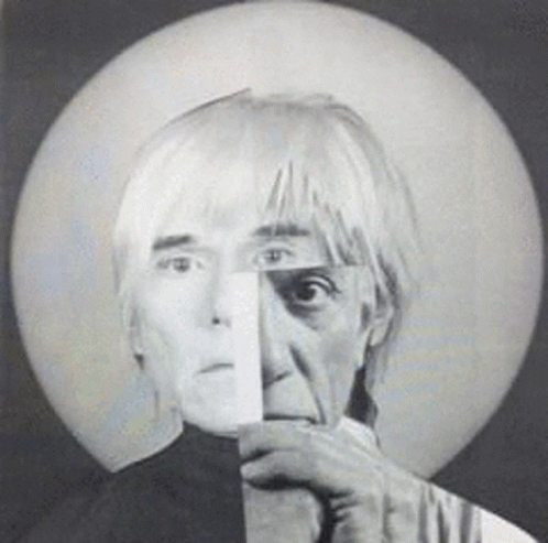 A Black And White Photo Of A Man Holding A Piece Of Paper To His Face GIF