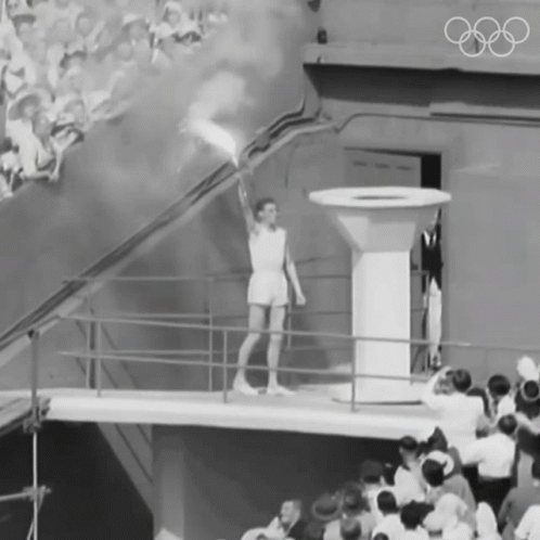 a black and white photo of a man holding a torch with the olympic rings on the wall behind him