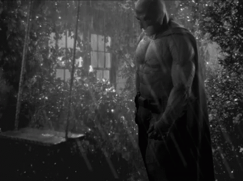 A Black And White Photo Of A Man In A Batman Costume Standing In A Room . GIF